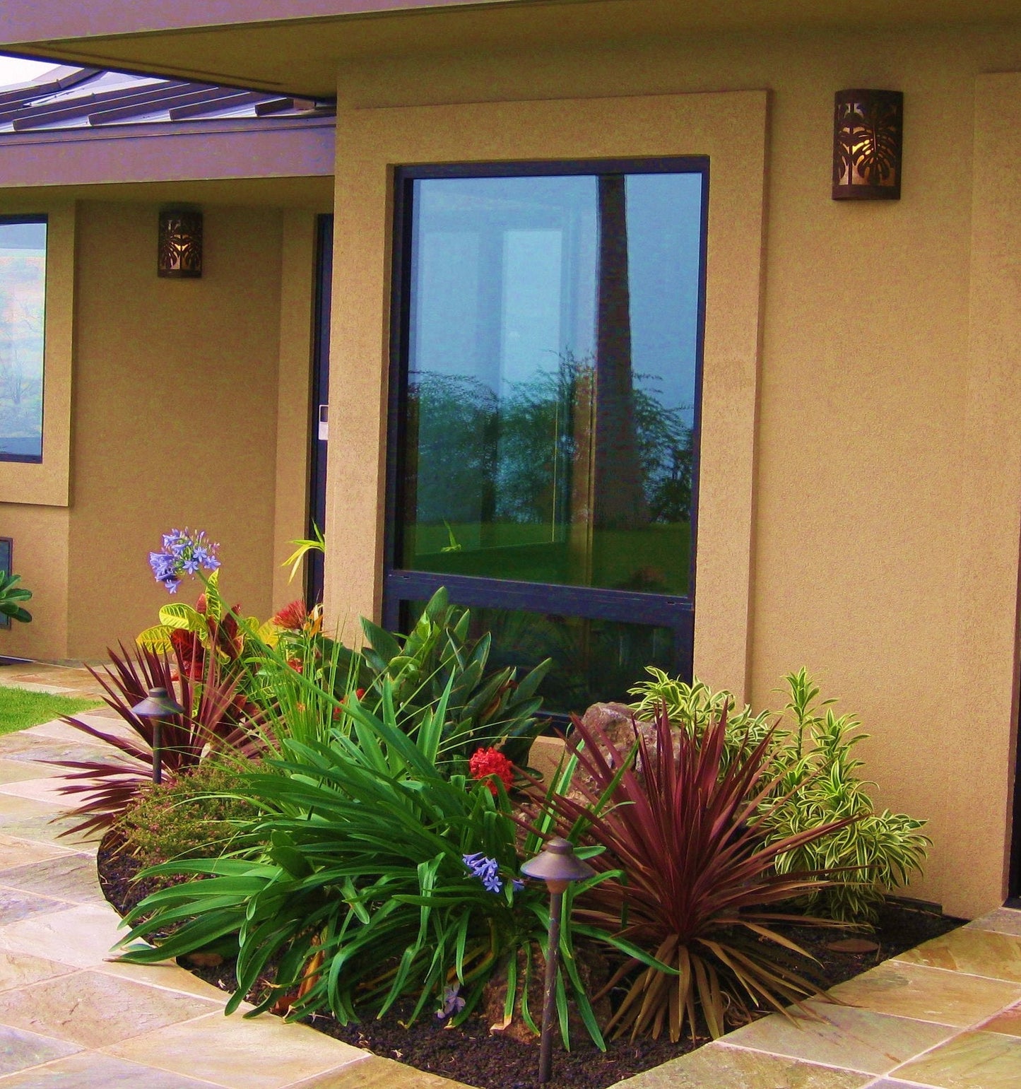 close up of scene with a window and a copper scone to the left with a palm tree reflecting in the window and a garden in the foreground