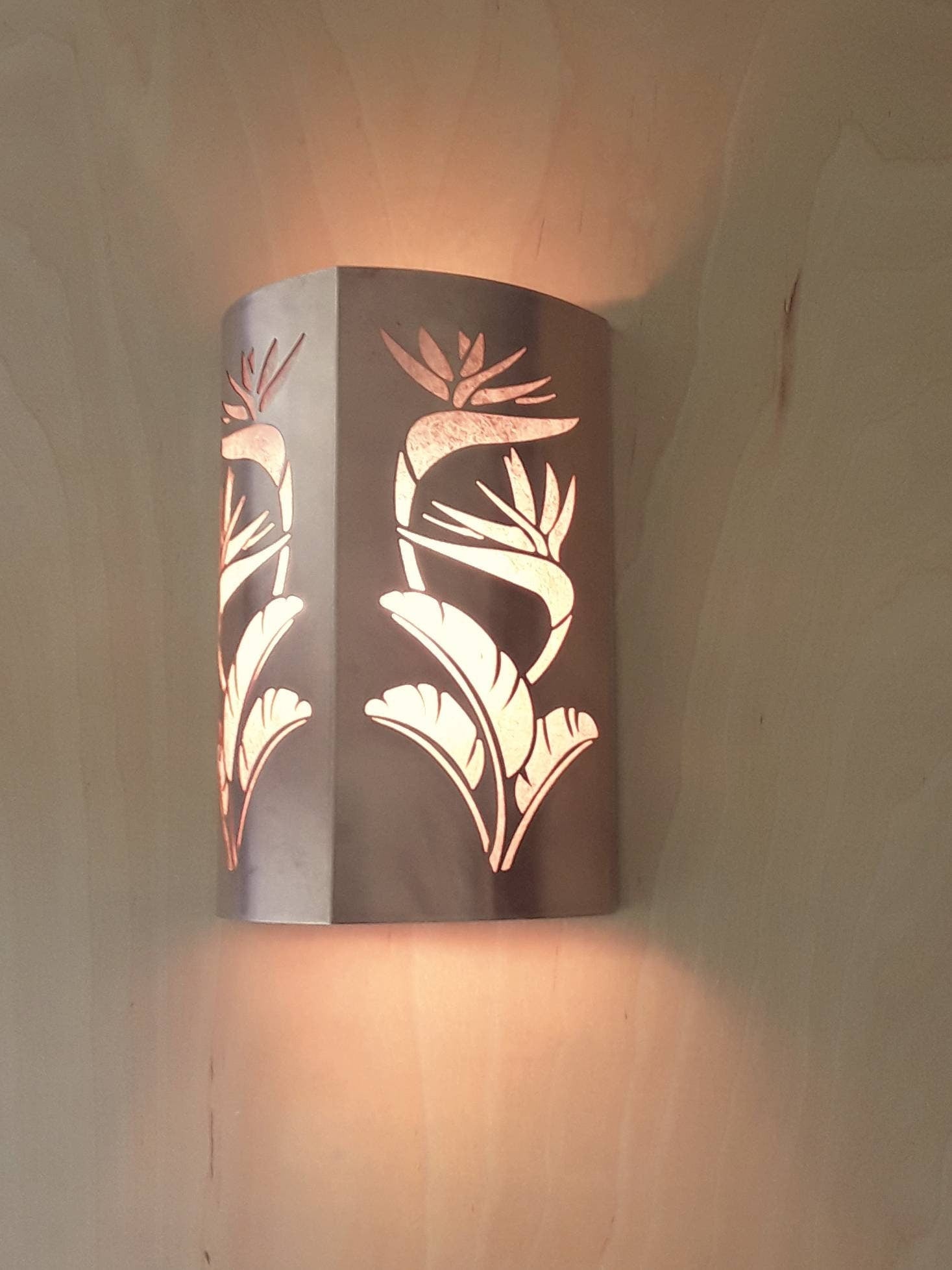side view of a copper sconce light with a double cut out of a bird of paradise design