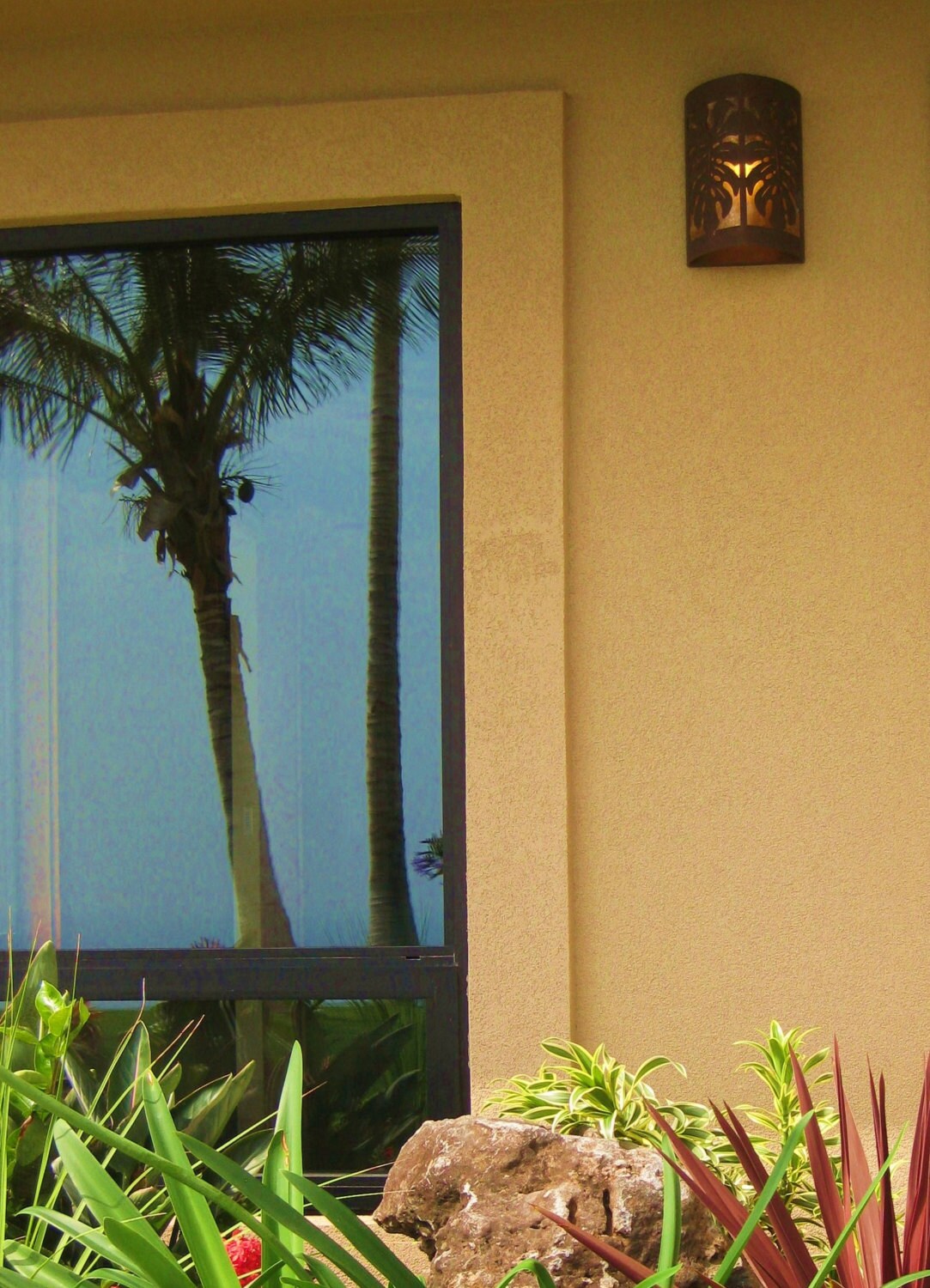 close up of scene with a window and a copper scone to the left with a palm tree reflecting in the window and a garden in the foreground