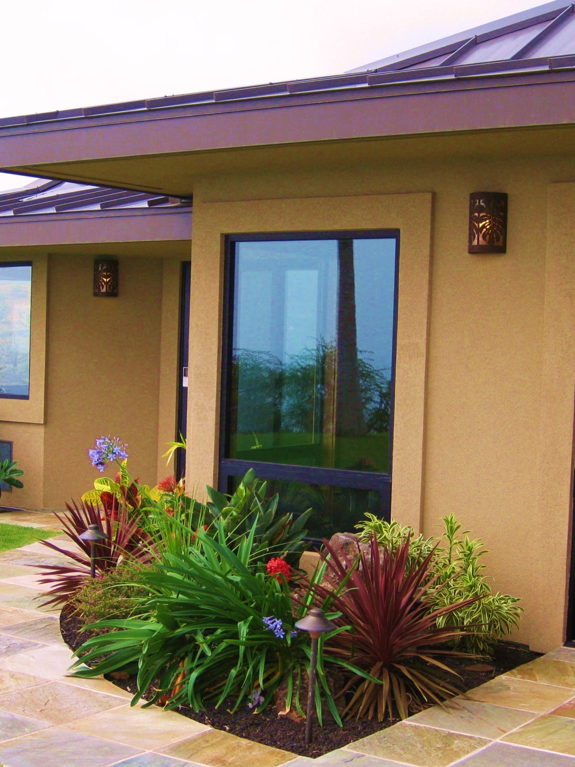 close up of scene with a window and a copper scone to the left with a palm tree reflecting in the window and a garden in the foreground
